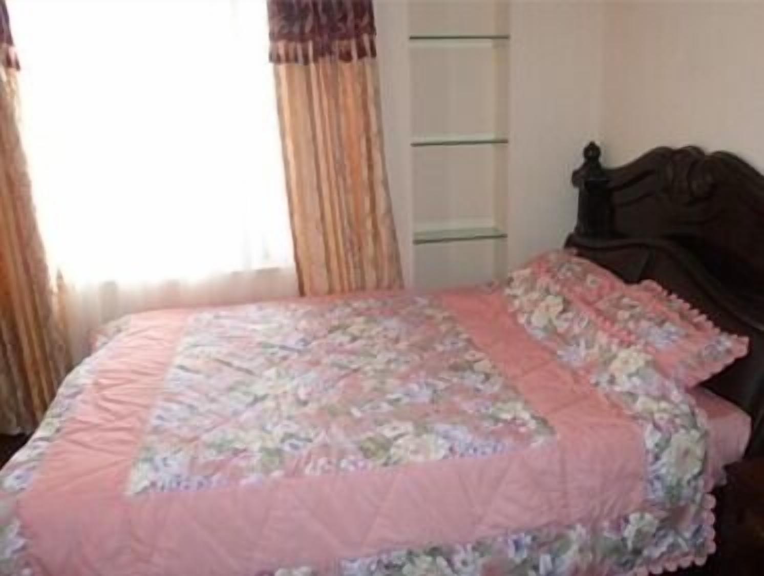 A bedroom with a bed, a window with curtains, and a wall-mounted shelf.