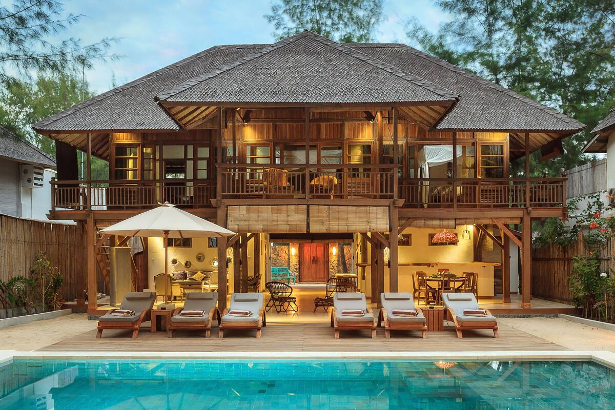 Une maison en bois à deux étages, dotée d’une piscine, de chaises longues et d’un coin repas.