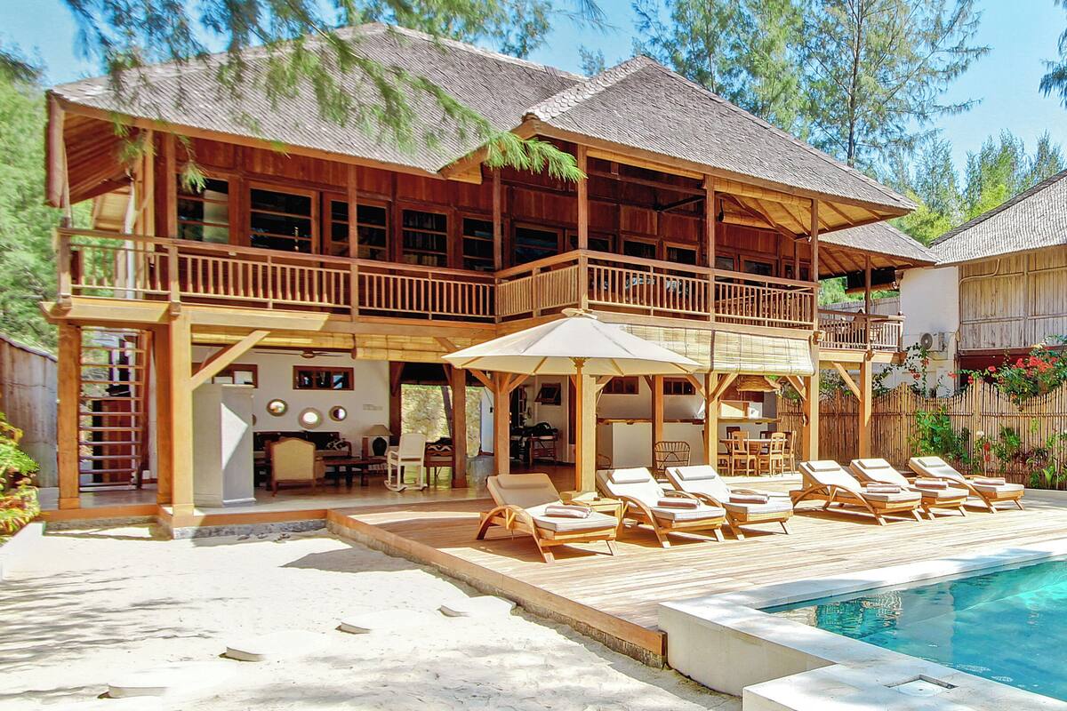 Une maison en bois à deux étages, dotée d’un balcon, d’une piscine et de mobilier d’extérieur.