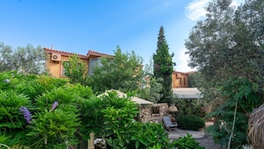 Un patio con un banco de piedra, una pérgola y una pequeña zona de cocina al aire libre.