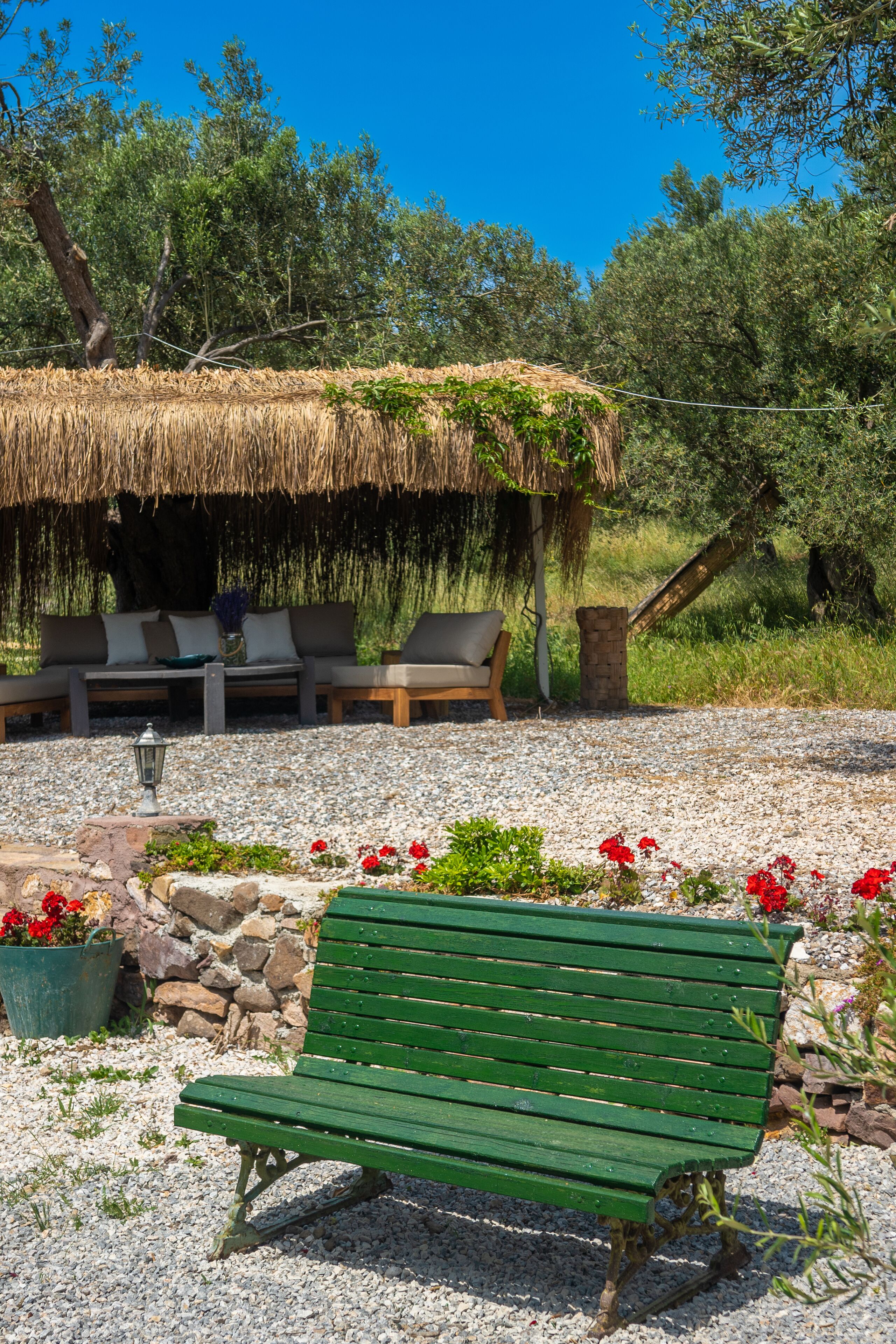 Un espacio de estar rústico al aire libre con techo de paja, un banco verde y una pared de piedra.