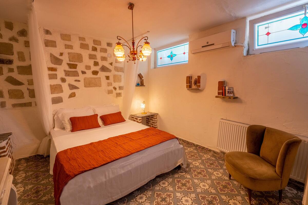 A bedroom with a bed, a chair, a stone wall, a window, and a radiator.