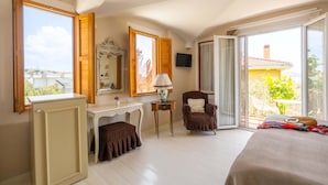 Un dormitorio con cama, escritorio, silla, televisor y ventanas amplias.