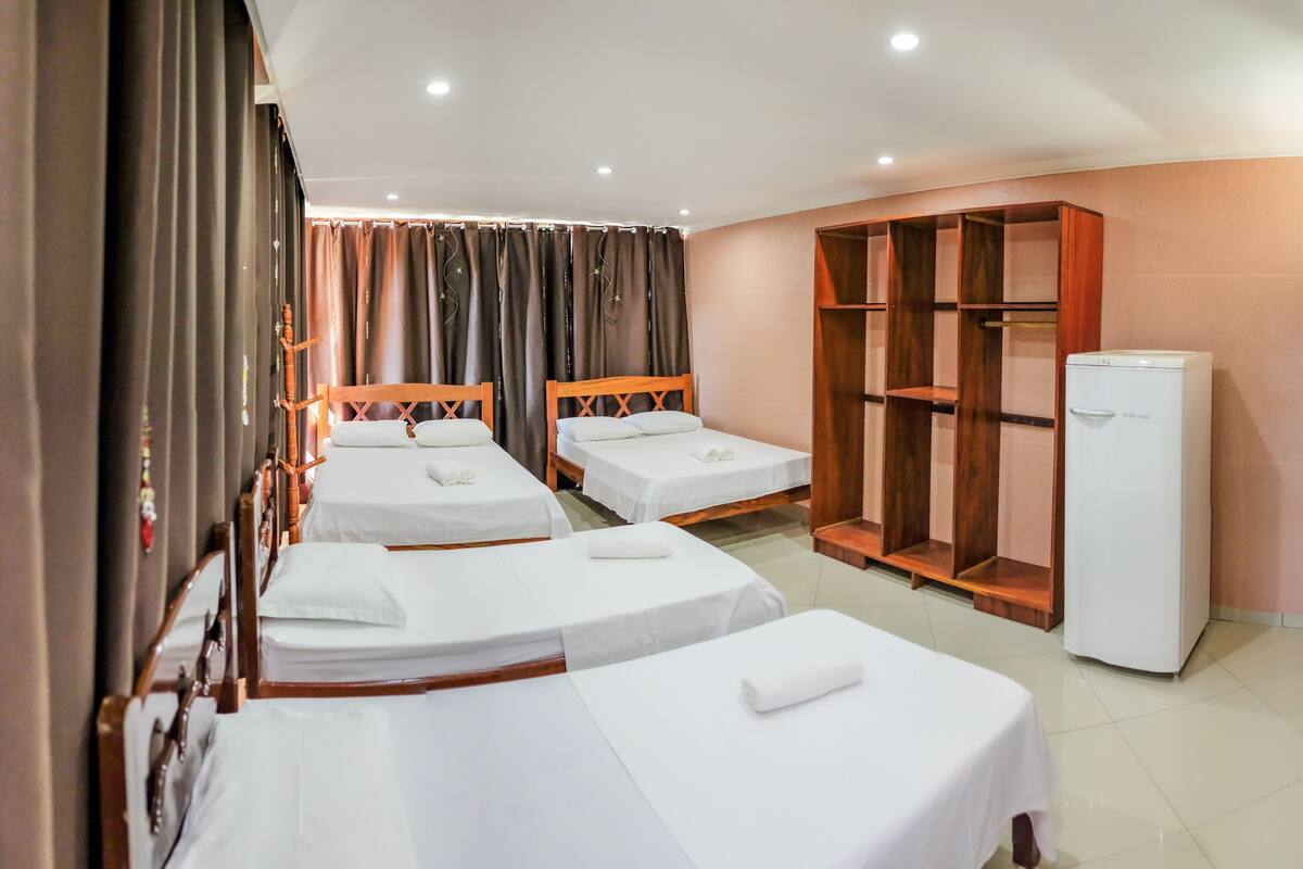 Quarto de hotel com três camas de solteiro, um guarda-roupa e um frigorífico.