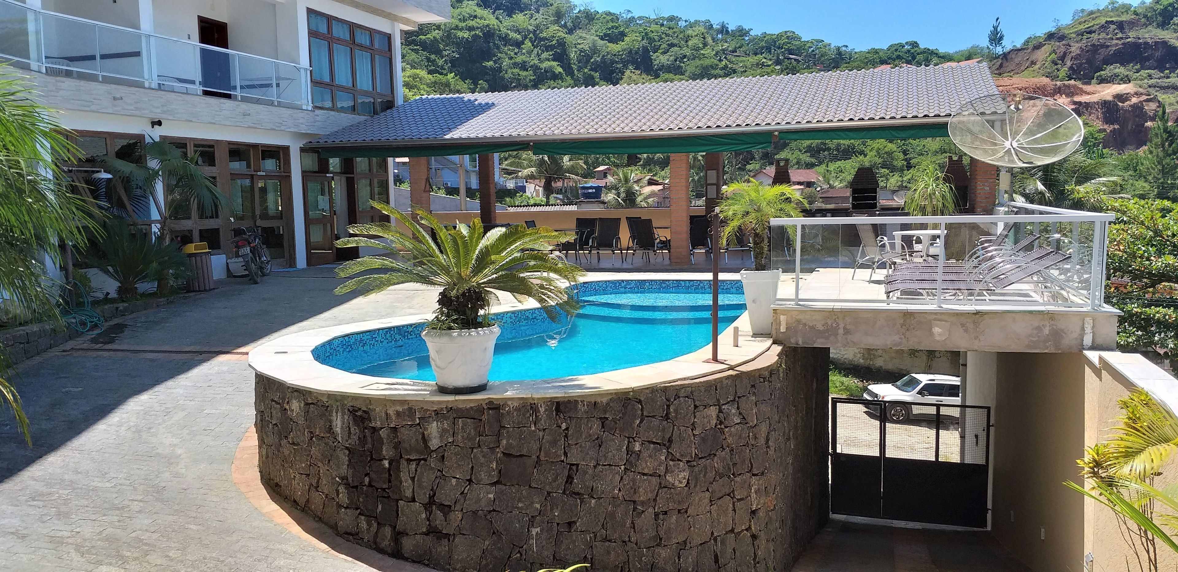 Una piscina con borde de piedra, rodeada de plantas en macetas y mobiliario de exterior.