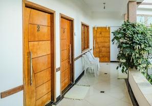 A hotel corridor with wooden doors numbered 1 to 4, white plastic chairs, and a potted plant. - Hospedaria Vitoria Mar (Ubatuba)