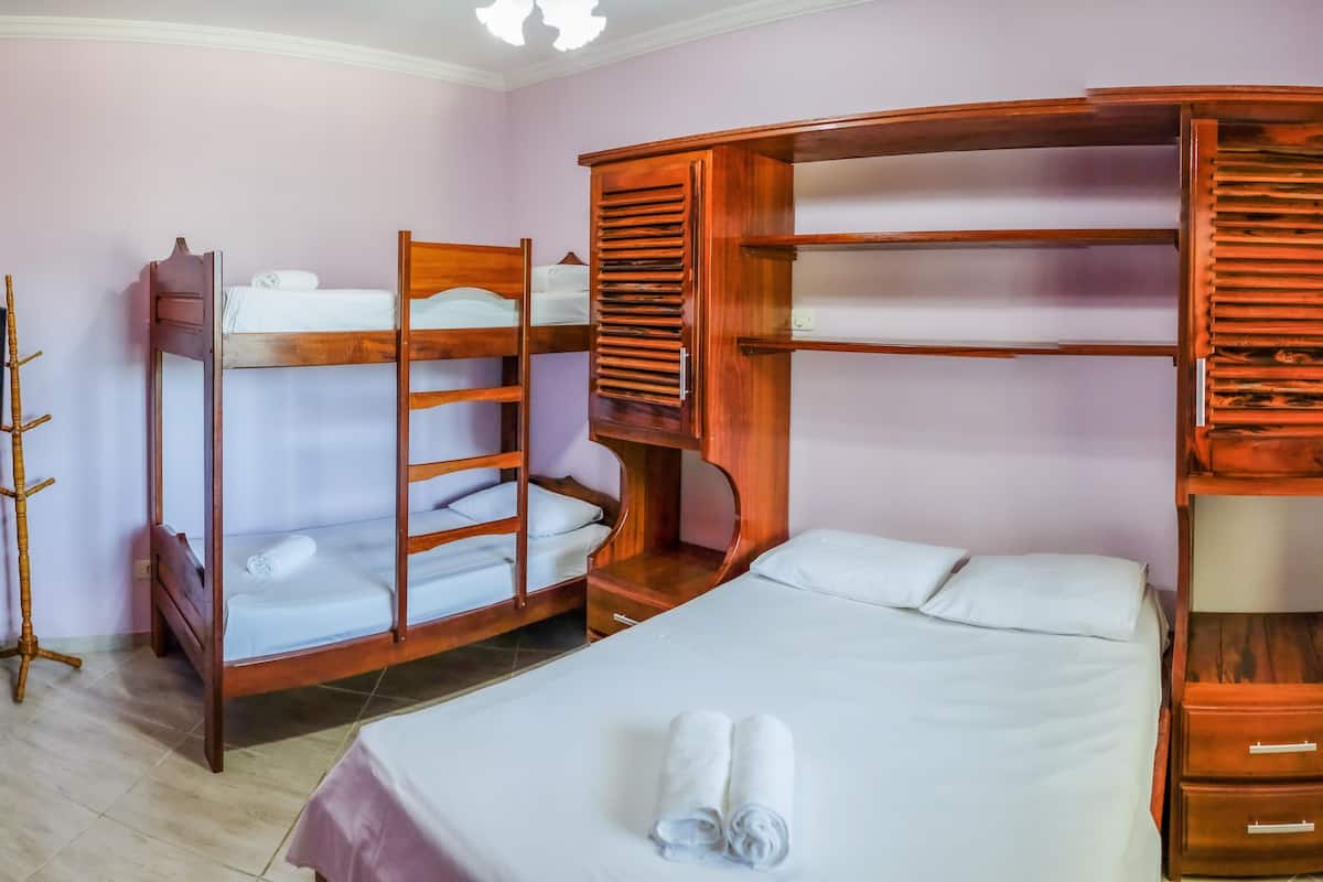Quarto com beliches, guarda-roupa, mesa de cabeceira e uma cama com toalha enrolada.