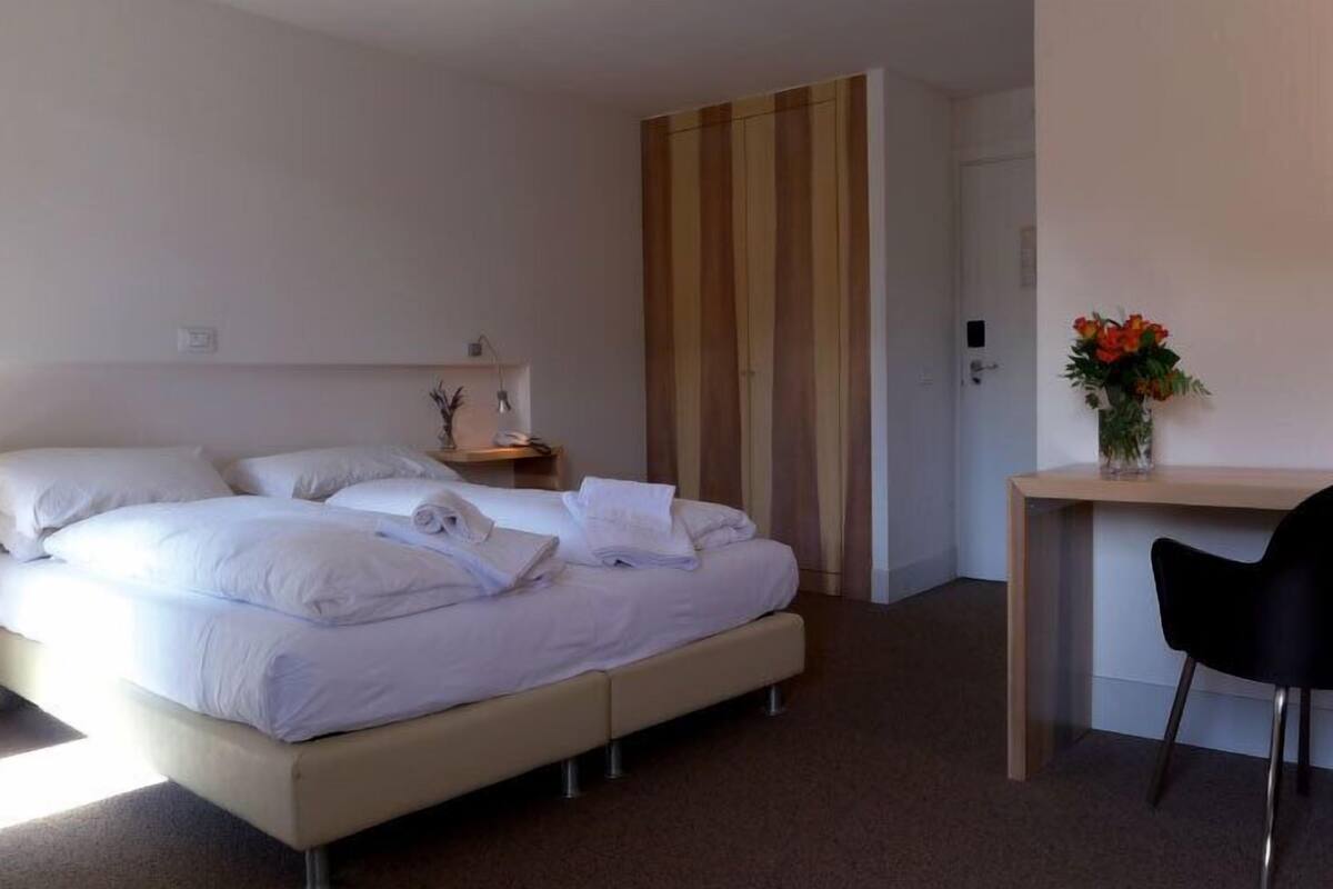 Une chambre d’hôtel comprenant un lit, une table de chevet, une lampe et un bureau avec une chaise.