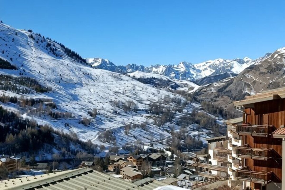 A mountain resort with snow-covered slopes, wooden buildings, and a clear sky.