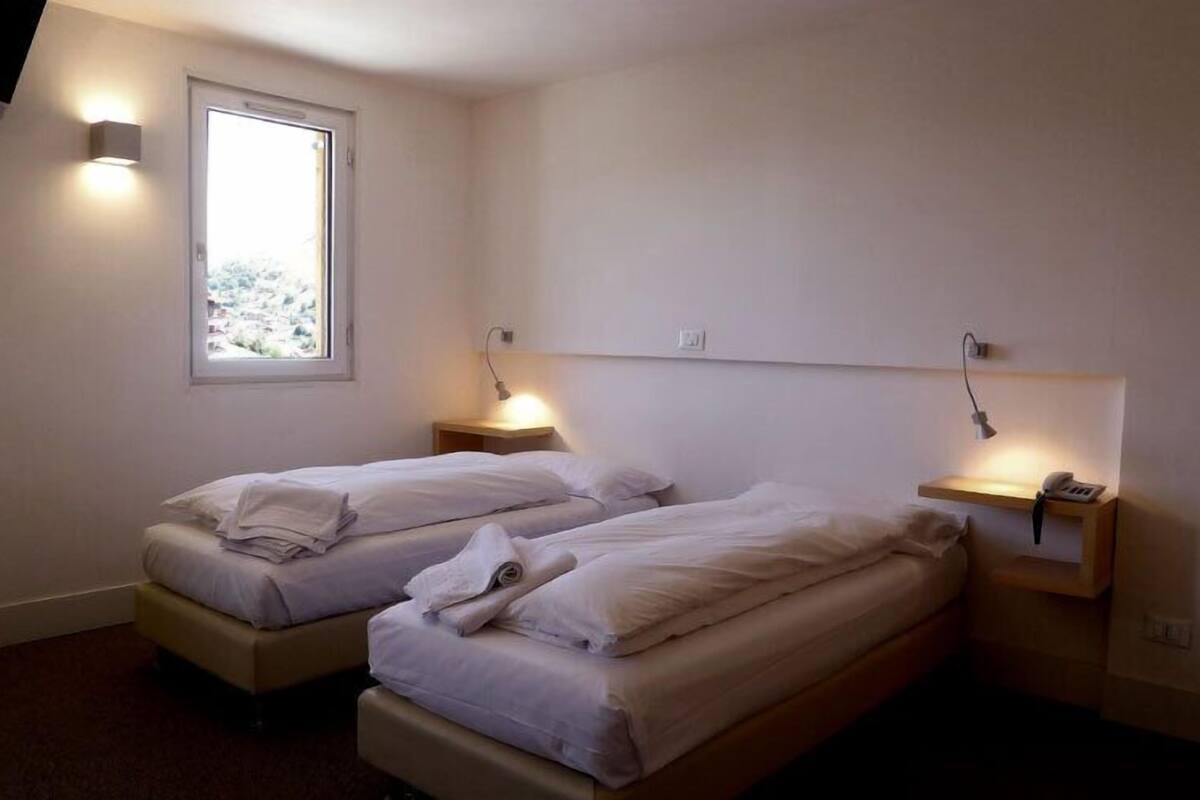 Une petite chambre propre, avec deux lits simples, une fenêtre et des lampes de chevet.