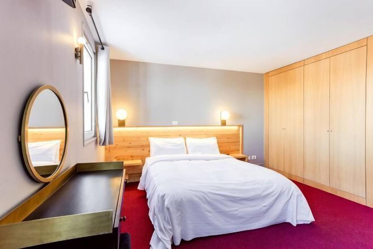 Une chambre d’hôtel équipée d’un lit, d’une table de chevet, d’un miroir, d’une armoire et de lampes fixées au mur.