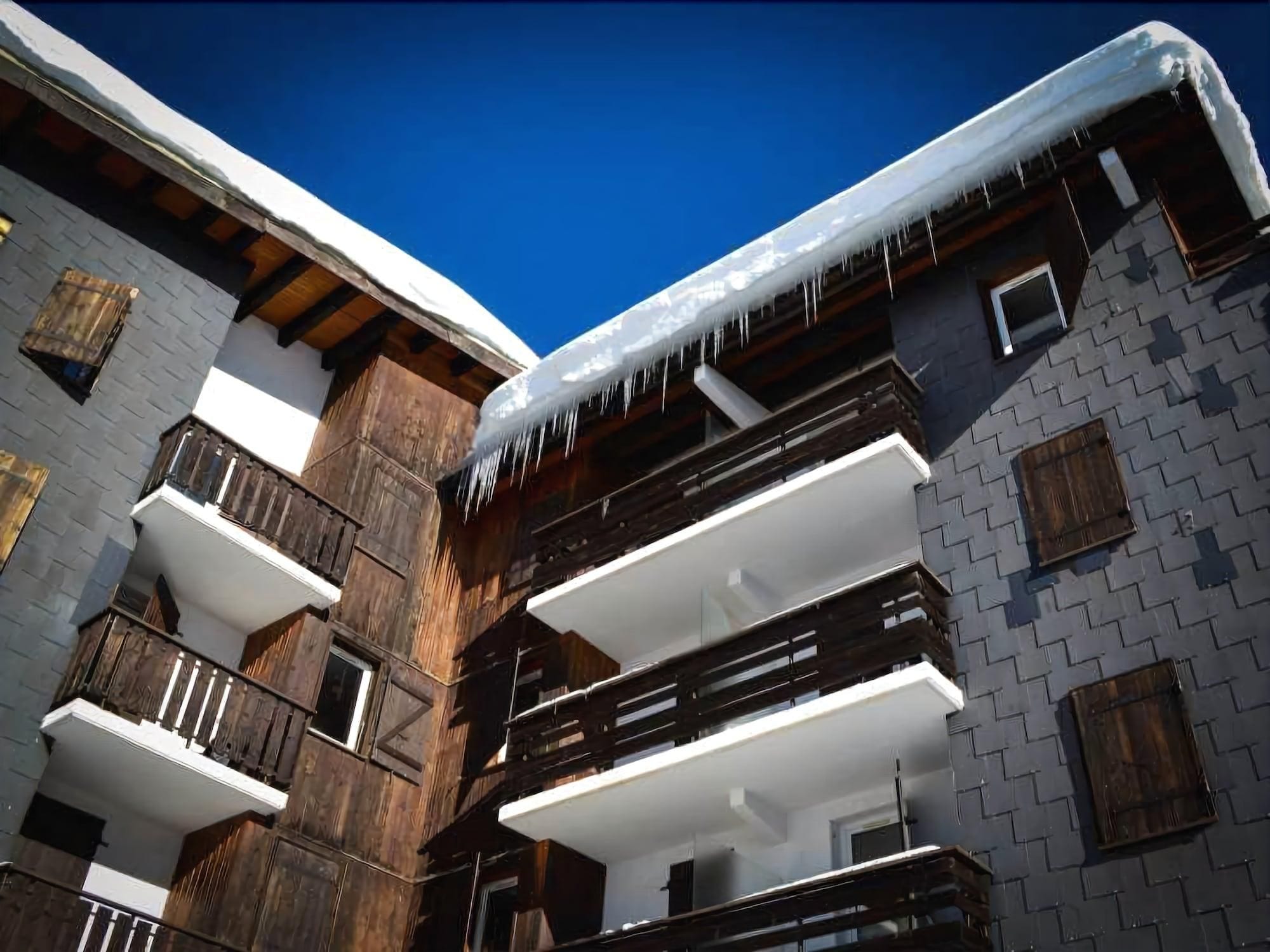 Un immeuble à plusieurs étages, doté de balcons en bois et de toits recouverts de neige.
