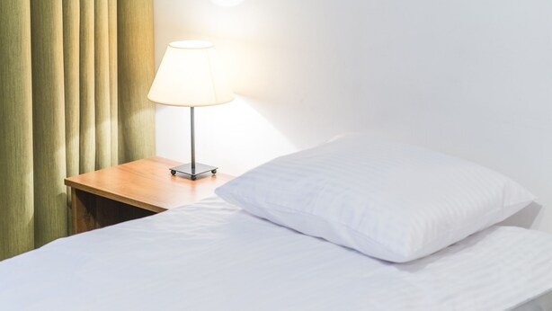 Una cama bien hecha con sábanas blancas, una mesita de noche de madera con una lámpara y cortinas verdes.