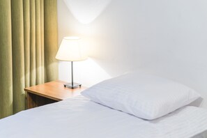 A neatly made bed with white linens, a wooden nightstand with a lamp, and green curtains. - SCSK Brzezno (Gdansk)