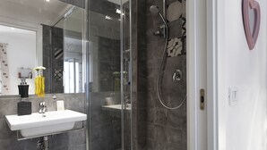 Un baño moderno con ducha acristalada, lavamanos blanco y espejo.