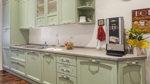 Una cocina con armarios verde claro, un refrigerador de acero inoxidable, una cafetera y un reloj en la pared.