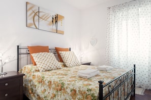 Una cama bien hecha con ropa de cama floral, un espejo con forma de corazón y un cuadro en la pared.