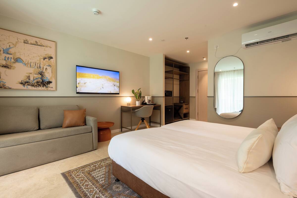 Ett modernt hotellrum med en stor säng, ett skrivbord, en soffa och en TV.