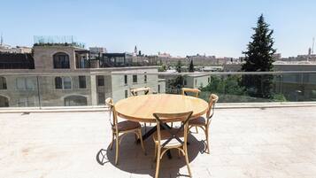 Una mesa redonda de madera con cuatro sillas en una terraza en la azotea, con vista a la ciudad.