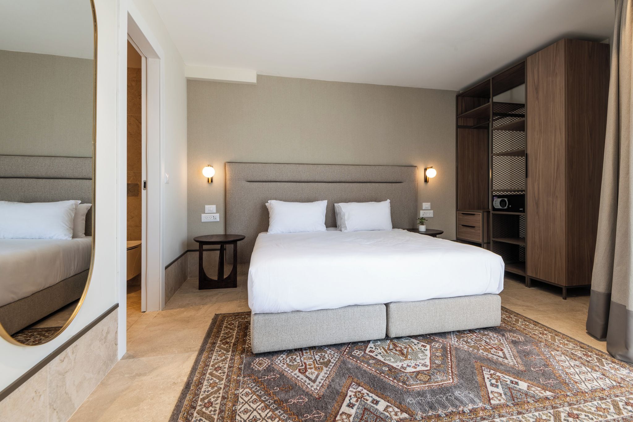 A hotel room with a large bed, bedside tables, a wardrobe, and a patterned rug.