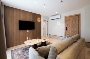 Una sala de estar moderna con un televisor de pantalla plana montado en la pared, un sofá color beige, una mesita de centro con dos botellas y una planta, y una alfombra estampada.