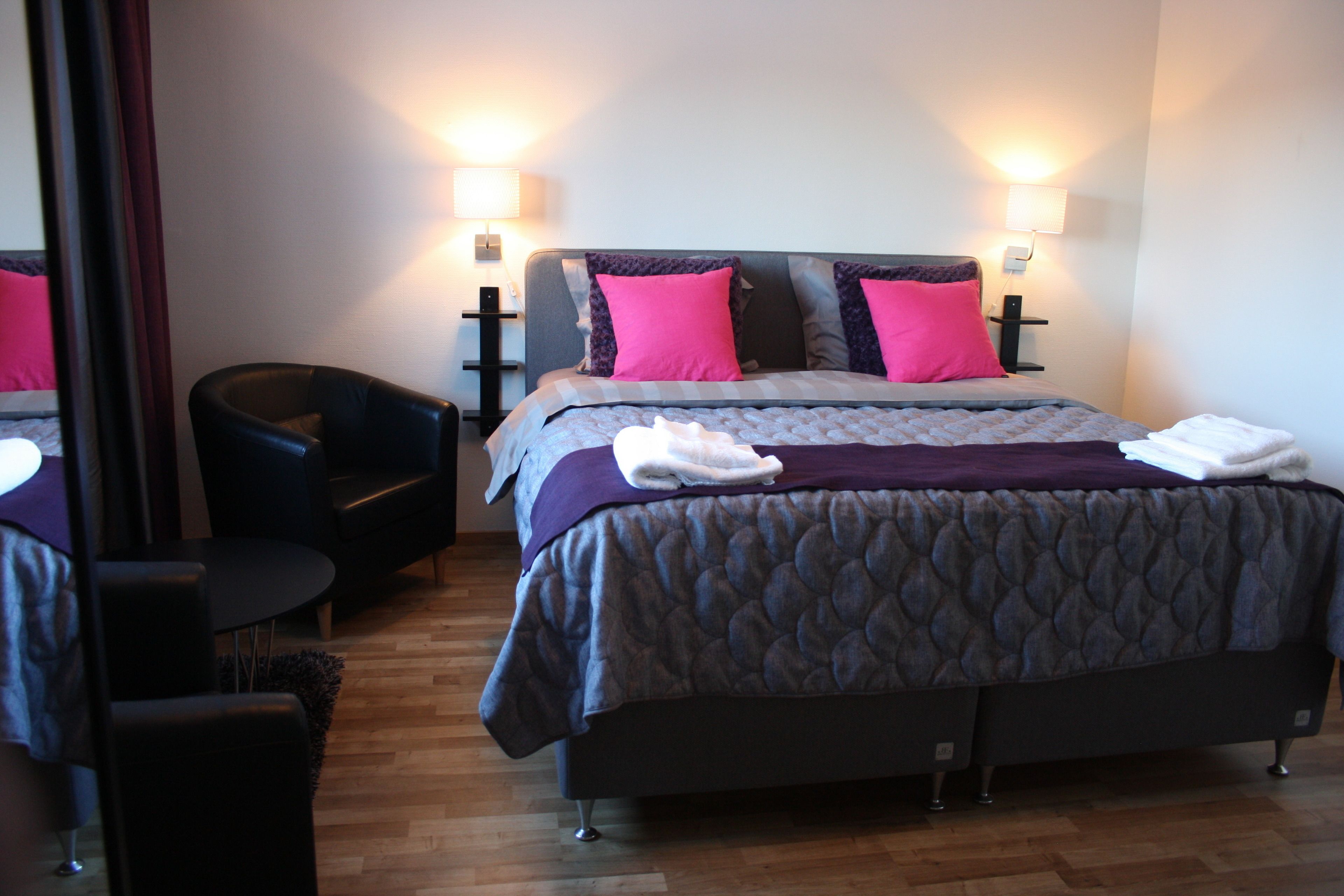 A neatly arranged hotel room with a large bed, two bedside lamps, a chair, and a wooden floor.