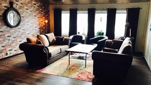 A cozy living room with a brick wall, a clock, and a large window with curtains. - Hotell Lyktan (Arjeplog)