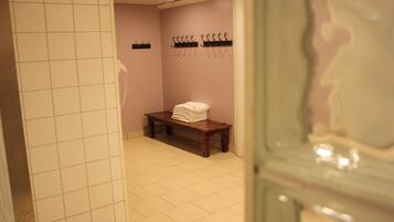 A bathroom with a tiled floor, a bench with folded towels, a telephone, and hooks on the wall.