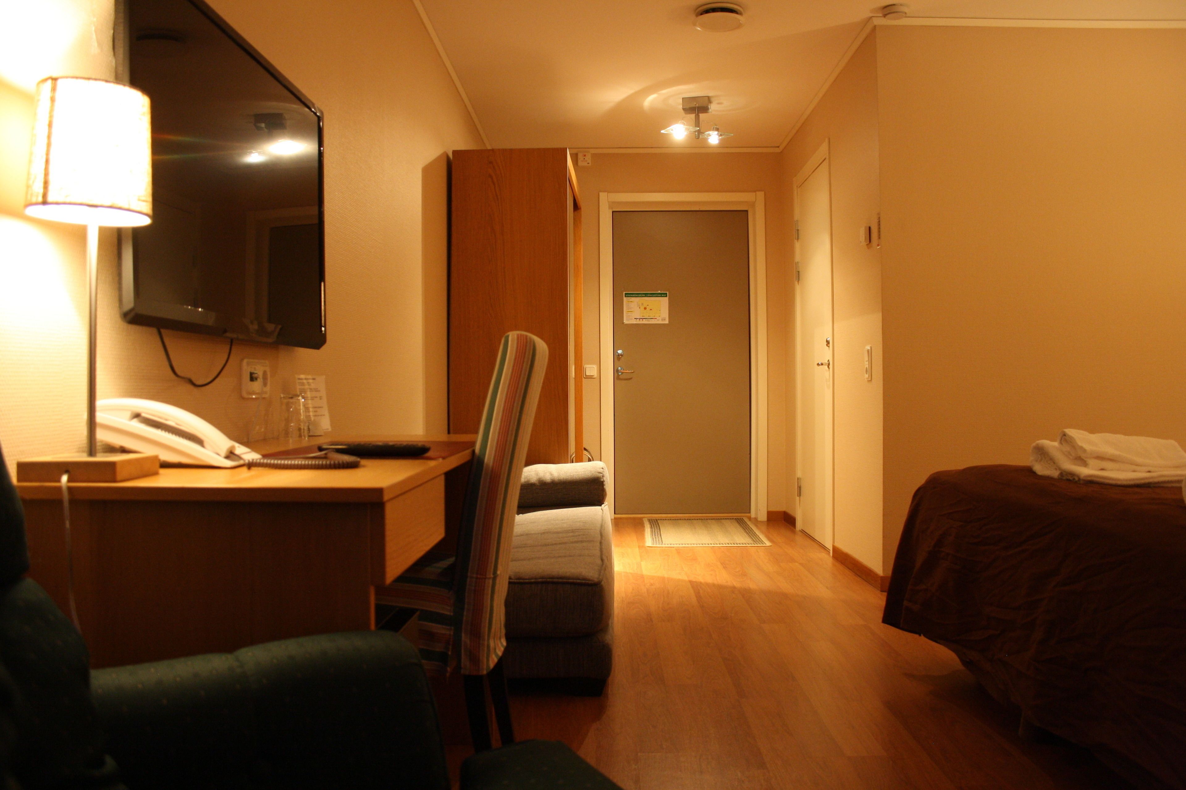 Ett hotellrum med ett skrivbord, en stol, en säng och en spegel.