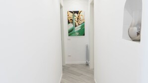 A narrow hallway with light-colored wooden flooring and white walls. There are recessed ceiling lights and a framed artwork on the wall. - Vantaggio Suites (Rome)