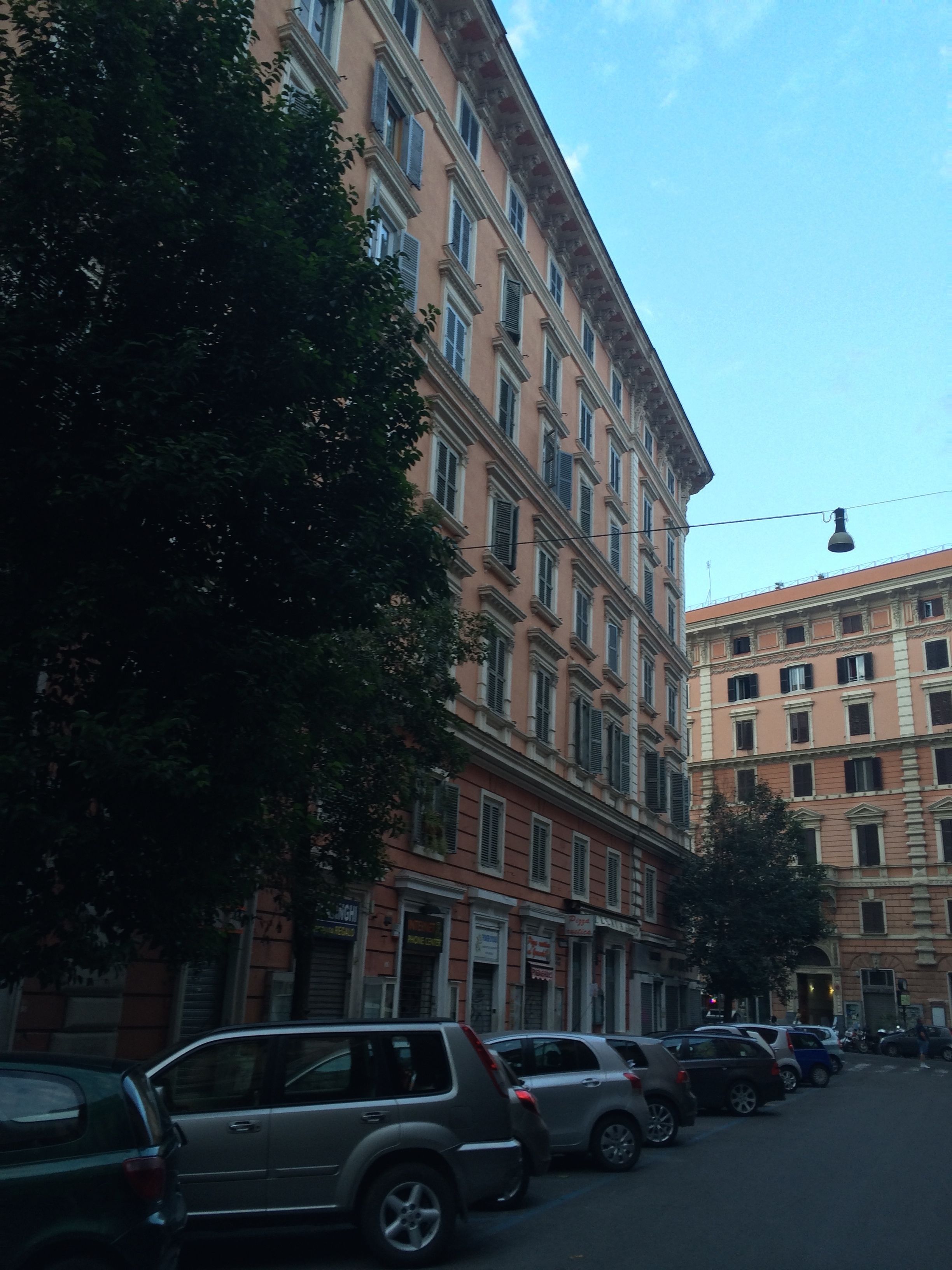 Filar de cotxes aparcats al costat d'un carrer flanquejat per edificis d'altures diverses.
