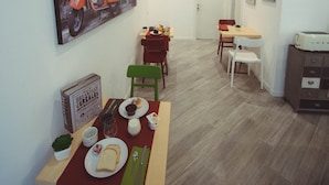 A dining area with a table set for two, a painting of a scooter on the wall, and a microwave on a cabinet. - Vantaggio Suites (Rome)