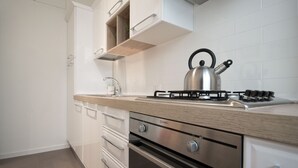A modern kitchen with white cabinets, a stainless steel kettle, and a gas stove. - Vantaggio Suites (Rome)