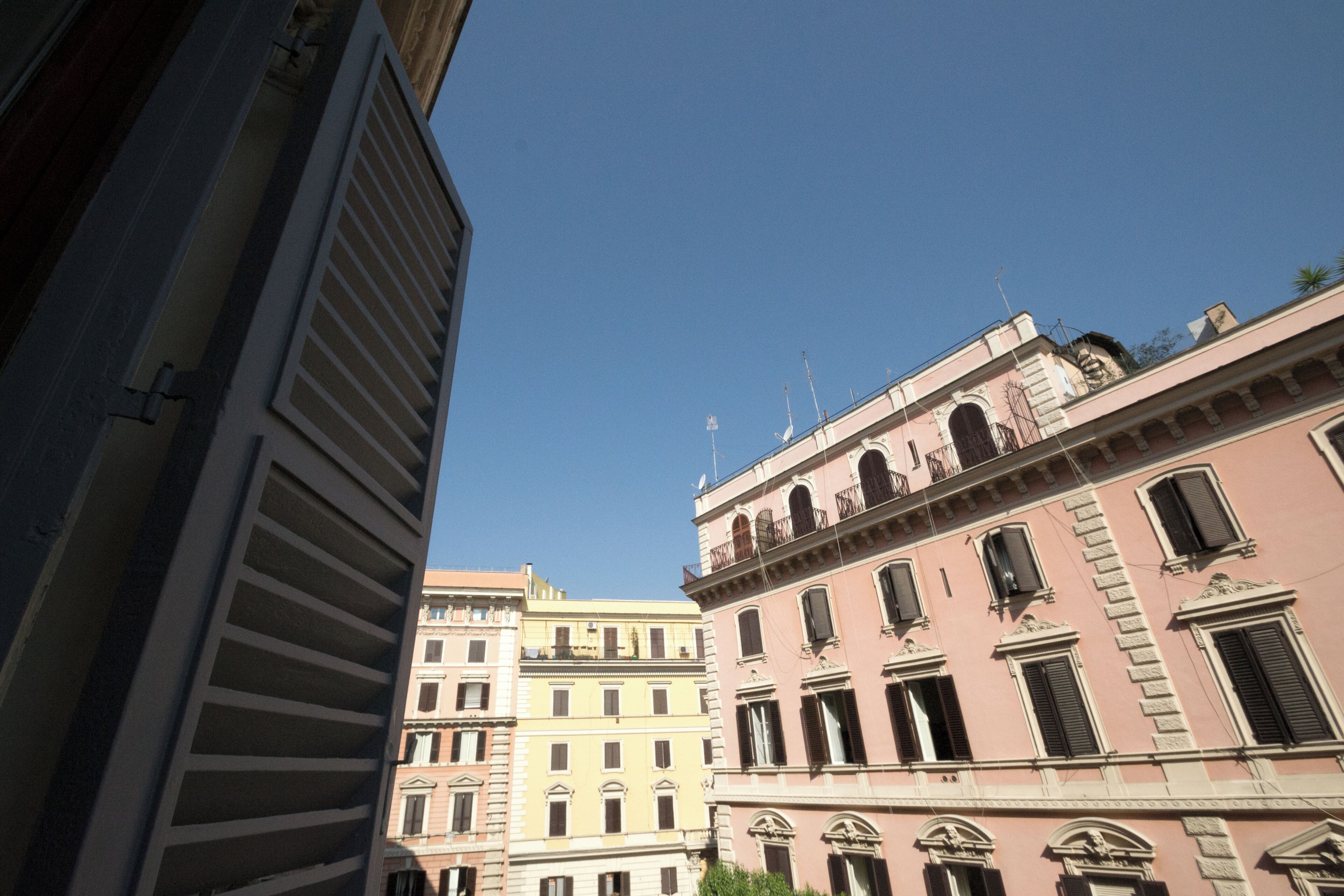 A narrow street with buildings on either side, featuring classical architecture with arched windows and balconies.