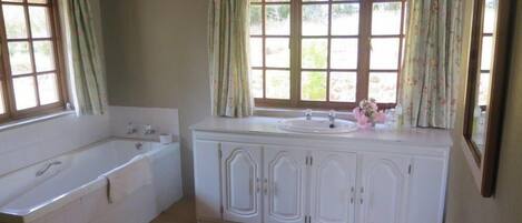 Une salle de bain avec une baignoire, un lavabo et un meuble. Il y a des fenêtres avec des rideaux.