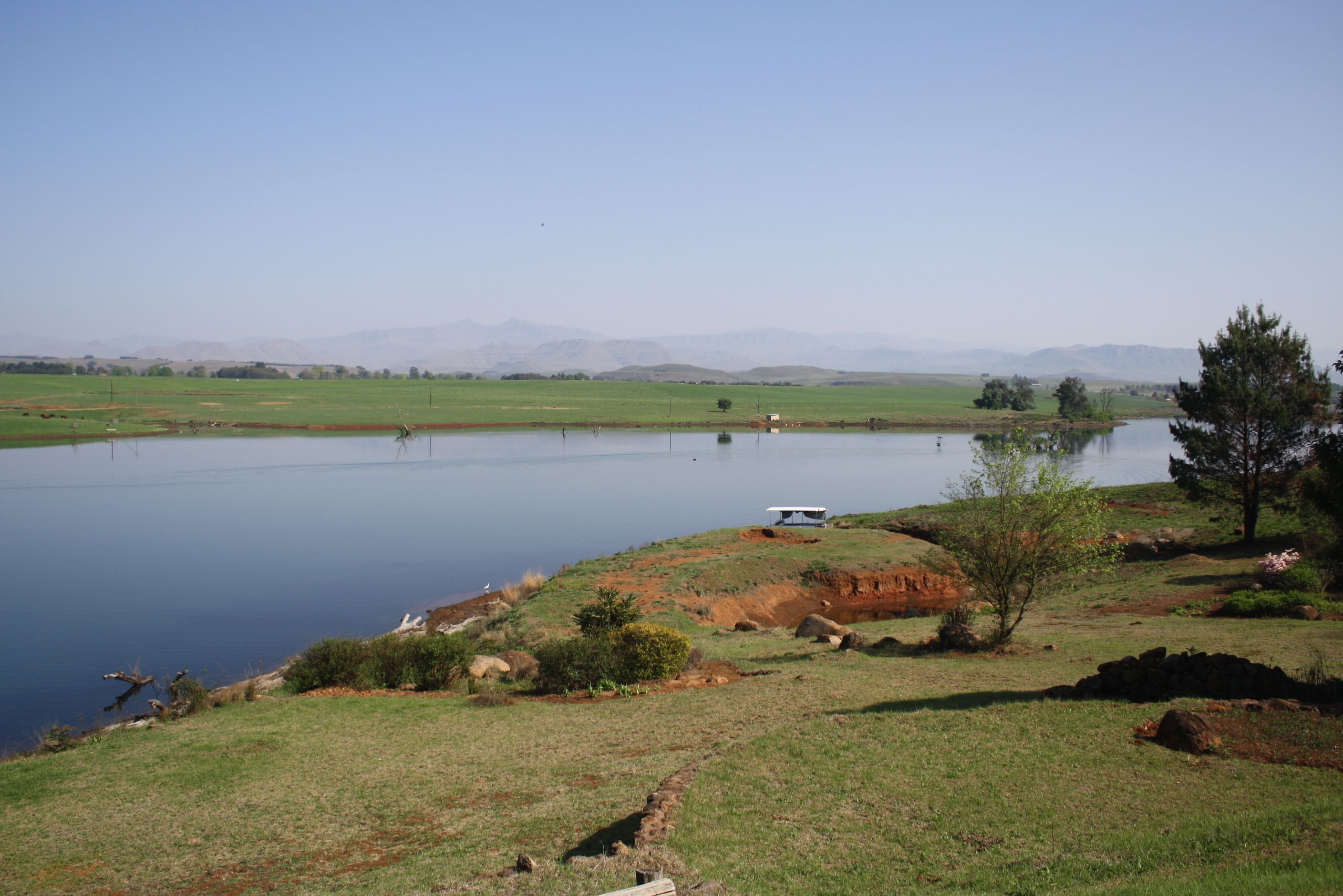A serene landscape with a lake, grassy fields, and distant mountains.