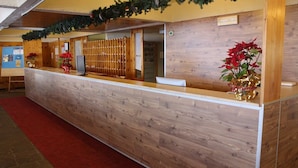 A reception desk with a wooden finish, two red poinsettia plants, and a red carpet. - TH 1400 (Mezzana)