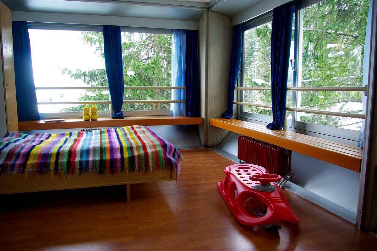 Une chambre à coucher avec un lit, un coin fenêtre, un radiateur et un parc pour enfants rouge.