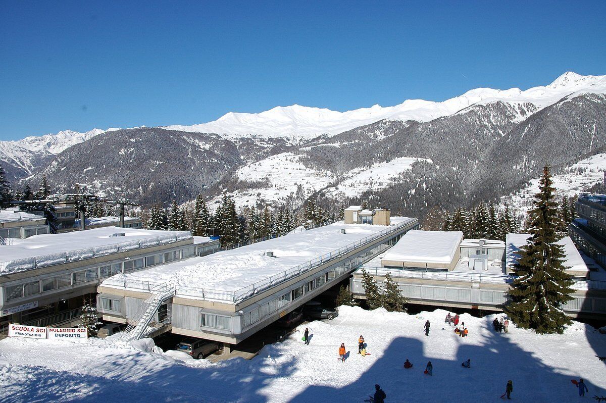 A snow-covered ski resort with a ski lift, buildings, and mountains in the background.