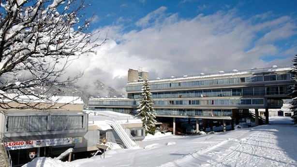 A multi-story hotel with a snow-covered ground and a clear sky. - TH 1400 (Mezzana)