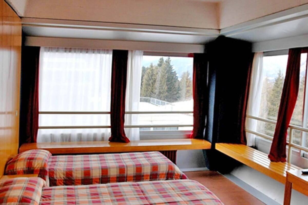 Une chambre à coucher avec un lit, un banc et une fenêtre avec des rideaux.