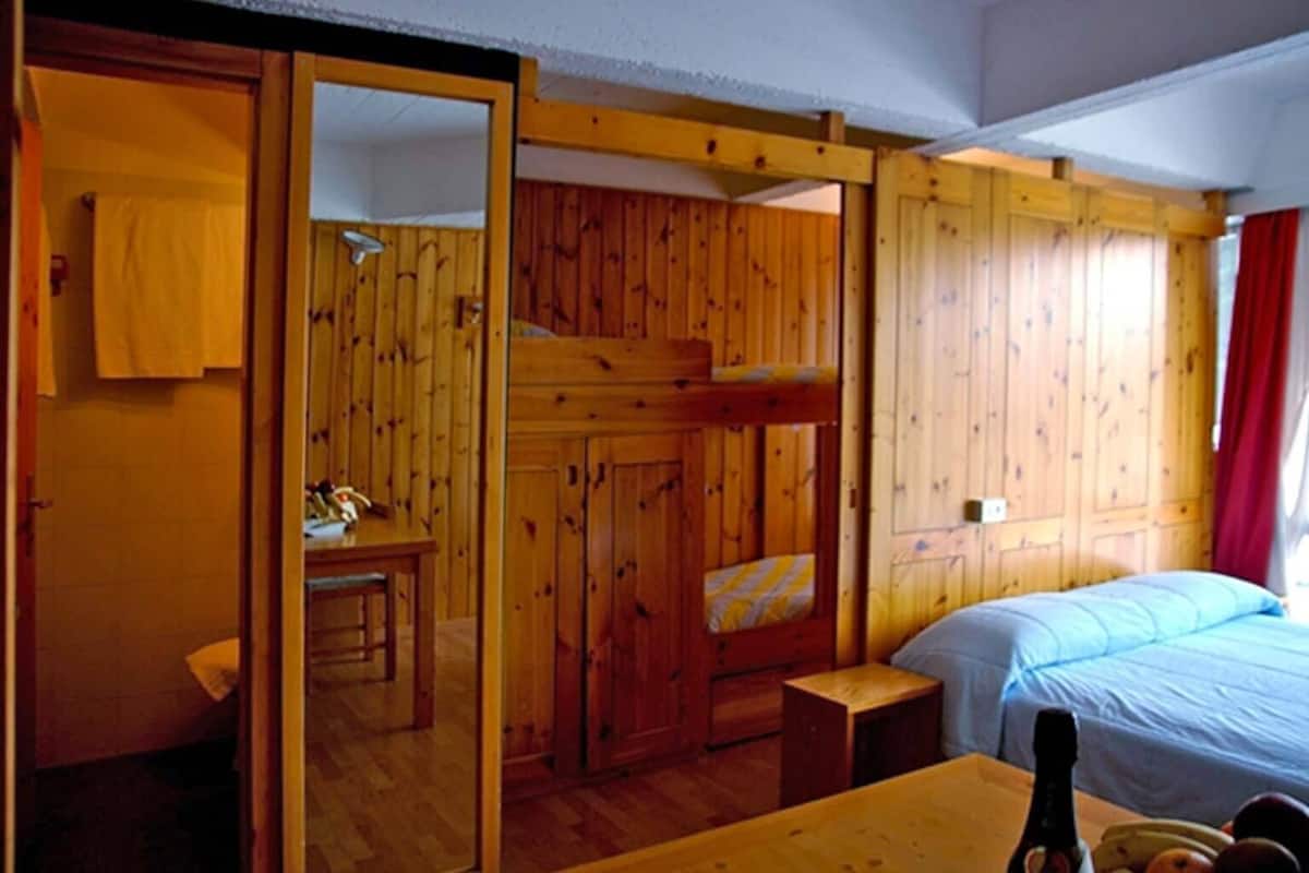 Une chambre dans un chalet en bois, avec des lits superposés, une petite table et un lit recouvert d’une couverture bleue.