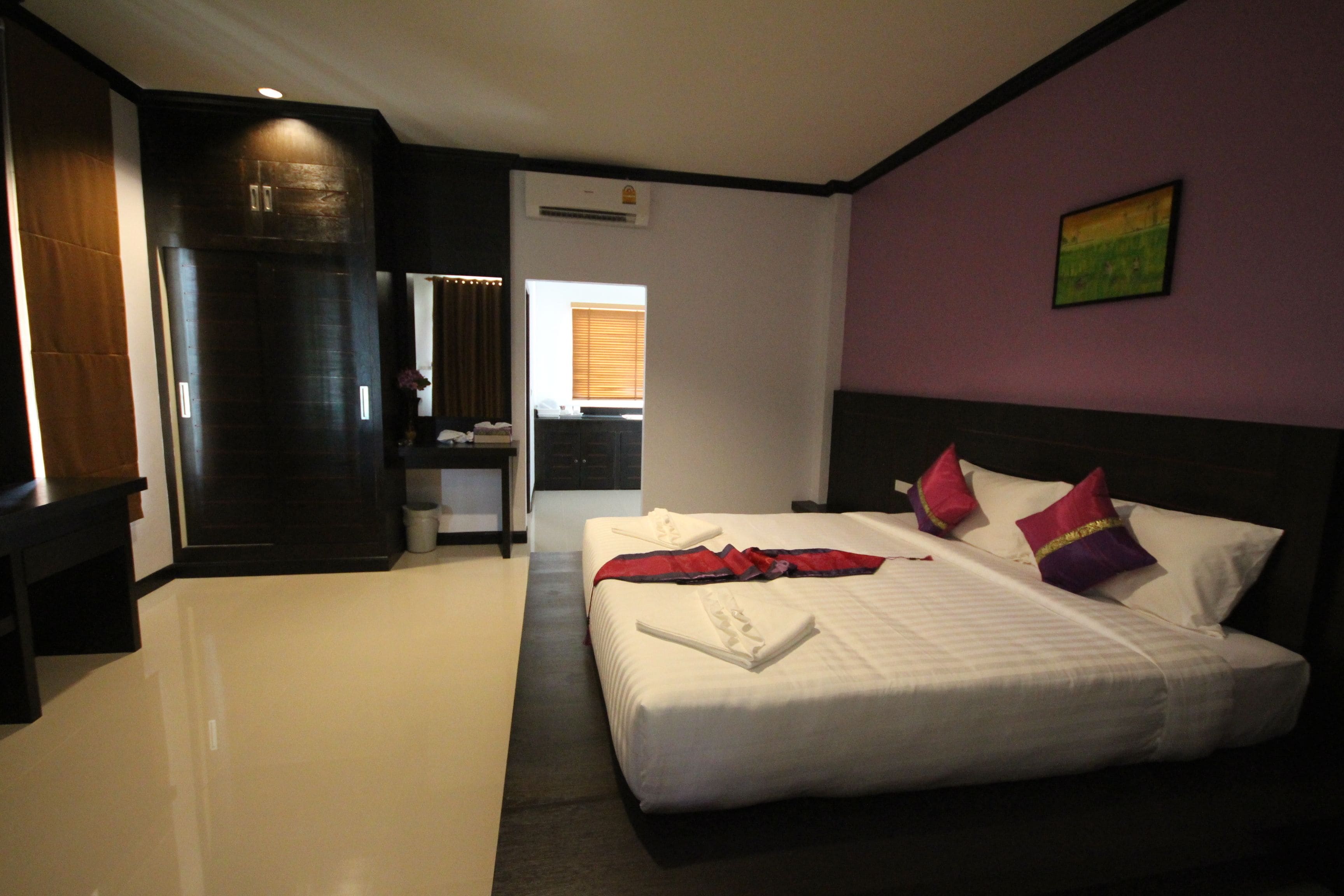 Een hotelkamer met een groot bed, een donkere houten garderobe, een klein bureau en een badkamer zichtbaar door een geopende deur.
