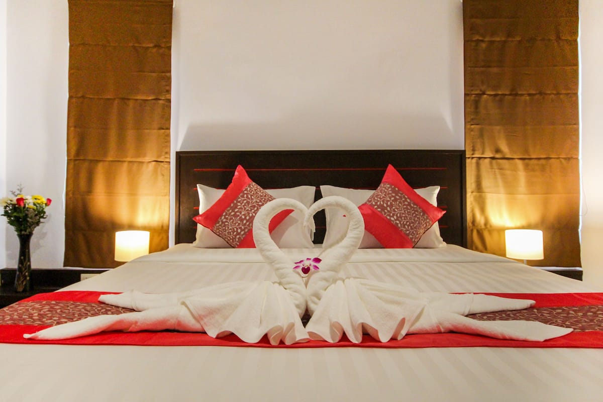 A hotel room with a neatly made bed, red and white pillows, and a decorative swan towel arrangement.