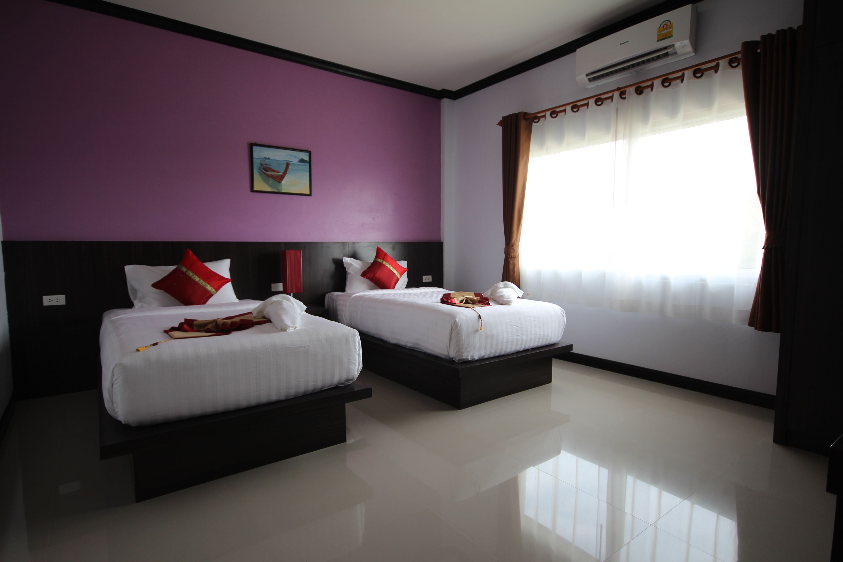 Habitación de hotel con dos camas, paredes moradas, un ventanal con cortinas y un equipo de aire acondicionado.