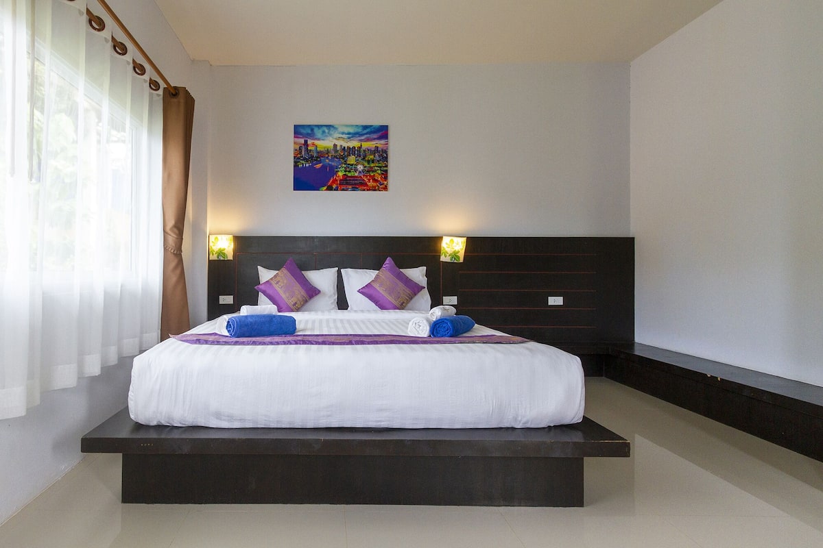 A hotel room with a large bed, dark headboard, and two wall-mounted lamps.