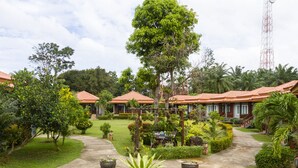 Un resort con varias construcciones, cada una con techo de tejas rojas y rodeada de exuberante vegetación y jardines bien cuidados.
