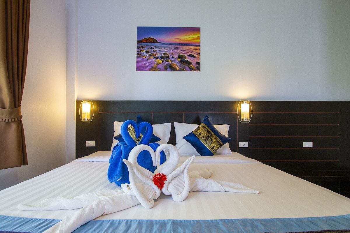 A hotel room with a bed, a painting of a beach scene, and two wall-mounted lights.