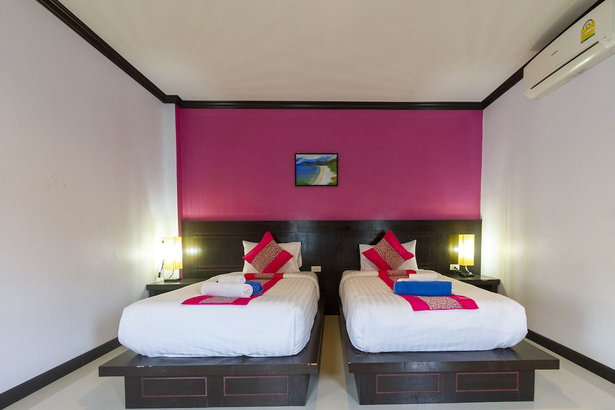 A hotel room with two beds, a dark headboard, a pink accent wall, and a small painting above the beds.