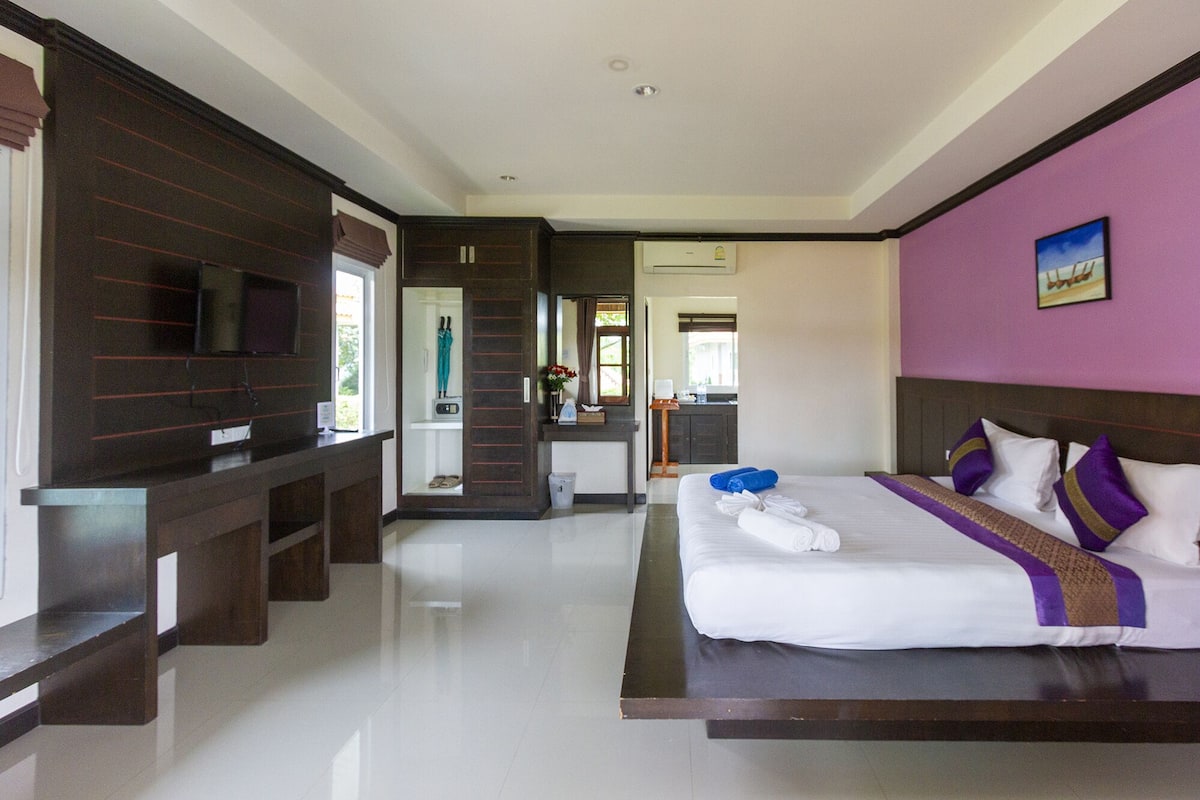 A hotel room with a large bed, a TV, a desk, and a bathroom visible through an open door.